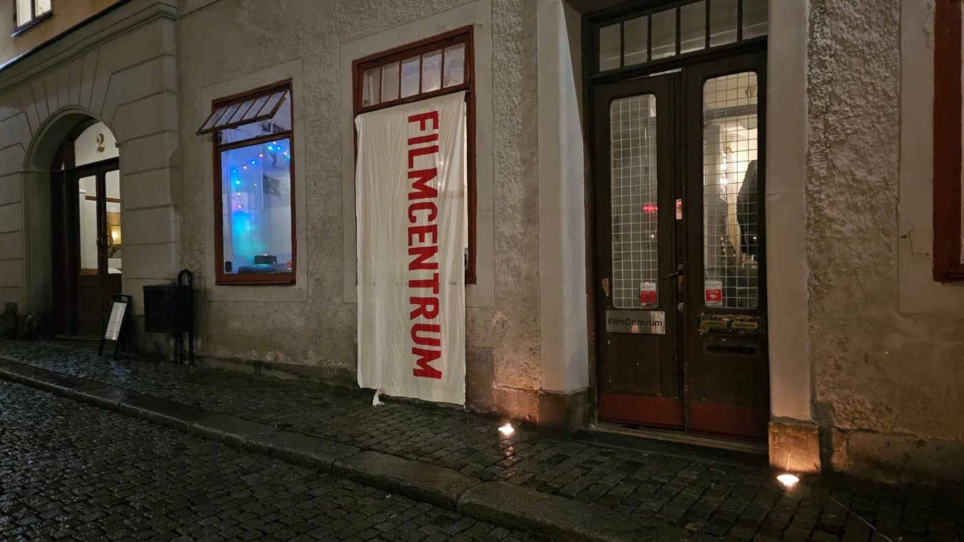 Filmcentrums lokal på Bredgränd 2 en kväll: en vit banderoll med texten FILMCENTRUM i fönstret och skylten FilmCentrum på dörren