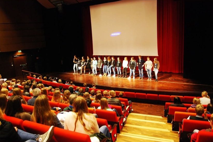 Skolelever i en full biosalong under MRF, en grupp står på scenen framför duken
